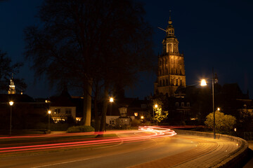 Fototapeta na wymiar Light streaks of passing cars on meandering town road lit up by city lights with Walburgiskerk cathedral towering behind into the night. Long exposure blue hour cityscape.