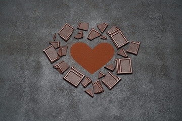 Heart shape made of grinded coffee or cocoa powder and pieces of chocolate bar on concrete background