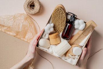 Beauty subscription Box preparation. Female hands holding gift box with natural skincare products, body brush, shampoo, soap, moisturizer. - obrazy, fototapety, plakaty