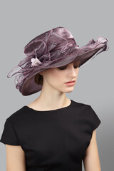 Romantic lady is wearing muted violet hat for evening party. Organza hat is decorated with large...