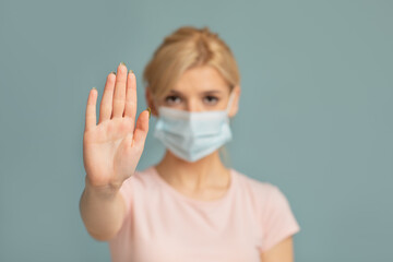 Stop worldwide COVID-19 epidemic. Woman in protective mask showing STOP gesture with open palm on grey studio background