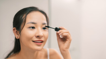 Young asian woman applying mascara in bathroom