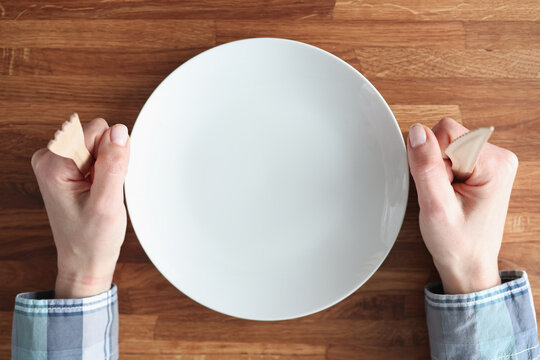 Female hands holding wooden fork and knife near white plate closeup