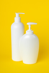 Obraz na płótnie Canvas Two plastic bottles on yellow background, set of cosmetic containers with a dispenser. Toiletries, pump lotion. Moisturizing cream for body and face. Liquid soap, personal hygiene concept, cleanliness