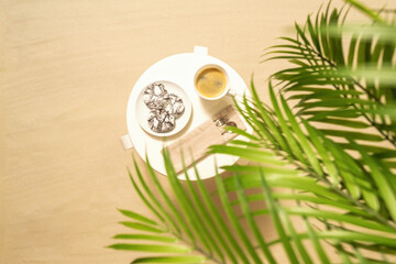 Cup of coffee with chocolate cookies on the table under palm trees on the sandy beach. Outdoors cafe. Top view