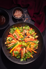 Colorful salad with fried chicken and a slice of carrot and zucchini on black background.