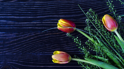 floral arrangement of red and yellow tulips with green leaves on a dark wooden background kopi space
