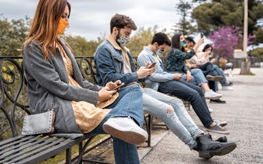 Technology concept of young people using smartphone in the park respecting the social distance due...