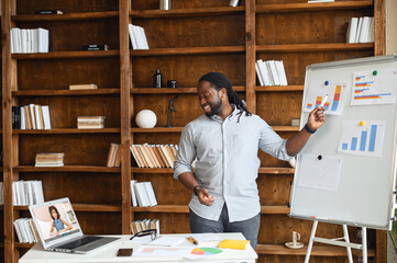 An African-American online teacher, tutor, business coach is holding webinar, points at whiteboard with graphs, explains to online audience on the laptop, biracial man makes a presentation online - Powered by Adobe