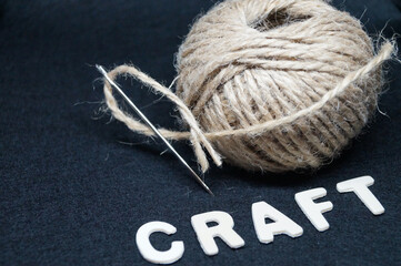 ball of natural coarse threads with a needle and the inscription wooden craft letters on a black background 
