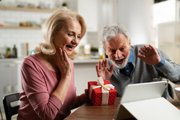  Senior couple having video call. Happy husband giving his wife a gift.
