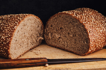 Loaf of bread sprinkled with sesame seeds lies on a cutting board with a knife.