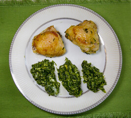 Chicken thighs with green spinach on a white round plate on a green napkin. Cooking healthy foods delicacies food.