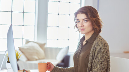 Young pretty woman having coffee and using laptop computer on sofa at home