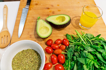horizontal view of mediterranean cooking ingredients on top of a wooden platter at home. Spanish breakfast preparation with avocado and fresh vegetables. Food and cooking concept.