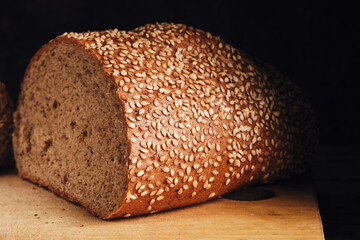 Bun sprinkled with sesame seeds lies on cutting board on dark background.