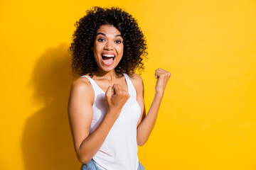 Photo of lucky charming young dark skin woman dressed white tank-top rising fists isolated yellow color background