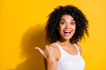 Photo of impressed dark skin woman dressed white tank-top pointing back thumb up empty space isolated yellow color background