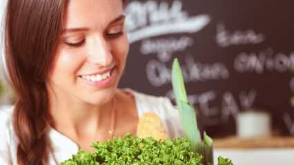 Smiling young woman holding vegetables standing in kitchen. Smiling young woman