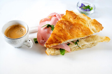 Pastry sandwich with salami and rucola, espresso and flowers on white.