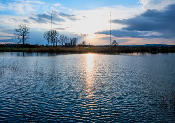 Blue lake surface and radio transmitter tower in illumination of evening sunset.