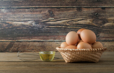 Farm fresh eggs in a basket on a wooden table. There is a wooden background.