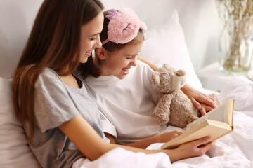 Happy woman and girl reading book on bed in morning