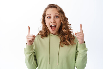 Surprised and excited woman gasping, pointing fingers up at top promo text, scream from joy and...