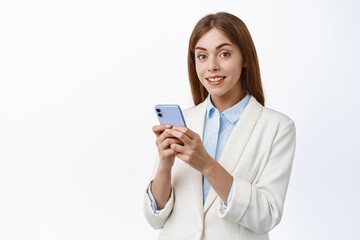 Girl in corporate suit hold smartphone and smiles at camera. Professional office woman using mobile phone, wearing business suit, white background