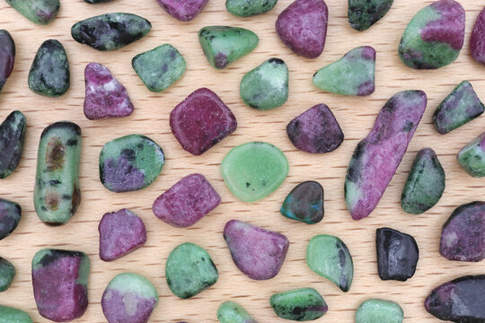 Ruby zoisite rare jewel stones texture on light varnished wood background.