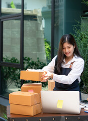 Young smiling beautiful owner asian woman freelance sme business online shopping working on laptop computer with parcel box on desk at home - SME business online and delivery concept