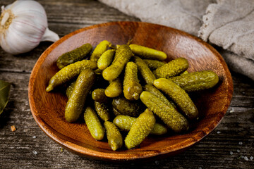 A bowl of pickled gherkins (cucumbers) on a rustic wooden background. Pickles