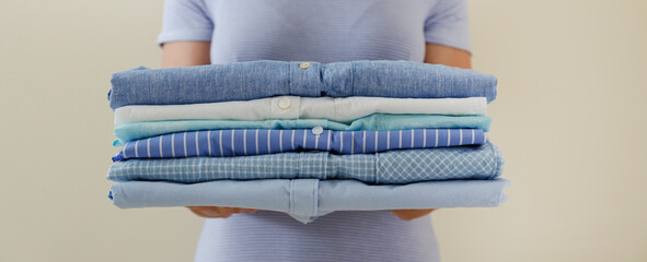 Cropped shot of young woman holding stack of perfectly folded shirts. Unrecognizable female with pile of different clothing in her hands. Laundry day concept. Close up, copy space, background