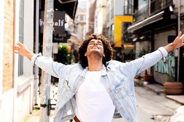 Obraz premium Young man enjoying outdoors. Handsome man with curly hair walking around town.