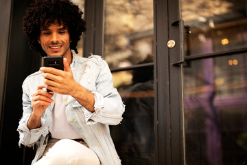 Young man enjoying outdoors. Handsome man with curly hair using the phone