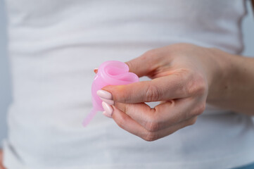 A faceless woman holds a folded pink menstrual cup. Alternative to tompons and pads