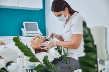 Young Caucasian redheaded female receiving professional face care in medicine center