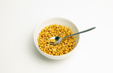 wheat flakes and tablespoon in a white cup on a white background