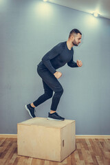 Man jumping onto the box on gray wall background. Athlete gave exercise. Jumping on the box. Phase touchdown. Studio shots in the dark tone.