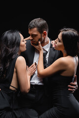 young man in suit near passionate women seducing him isolated on black.