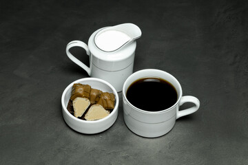 black coffee in a white cup, milk in special dishes and chocolates in a small white saucer on a gray background