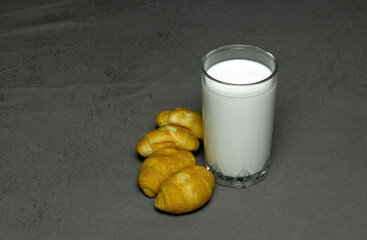 milk in a clear glass and four croissants on a gray background