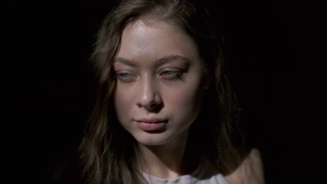 Close-up of girl with long light brown hair and grey eyes drinking coffee with pleasure from a white cup. Filmed in full face on a black background