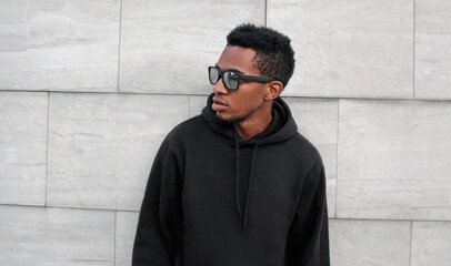 Portrait of stylish young african man posing looking away wearing a black hoodie, sunglasses on a...