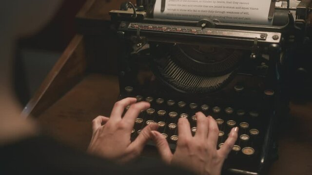 Cinematic over the shoulder shot of woman typing on vintage typewriter