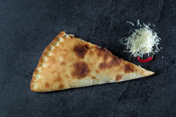 pie or closed pizza with cheese on a dark gray stone background