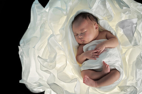 Newborn was wrapped in swaddling cloth sleeping on a white paper flower on black background.