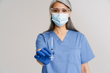 Asian mature woman in medical uniform and face mask holding syringe