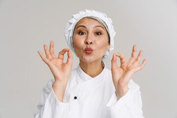 Asian mature woman in white chef uniform doing tasty delicious gesture