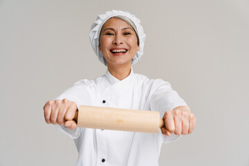 Asian mature woman in chef uniform smiling and holding rolling pin